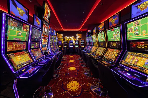 A woman smiling by bright slot machines showing lucky symbols, showcasing the exciting slot offerings at KK333BD.